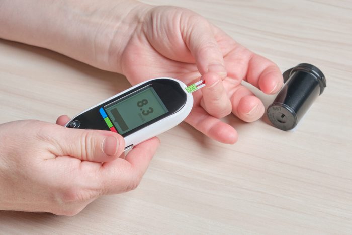 a senior woman with diabetes checks her blood sugar level with a glucose meter, a drop of blood on her finger, a high sugar level on the screen of a digital glucose meter