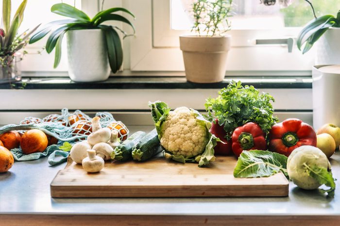Kitchen table with various fresh vegetables , cutting board and sustainable shopping mesh bag at window background